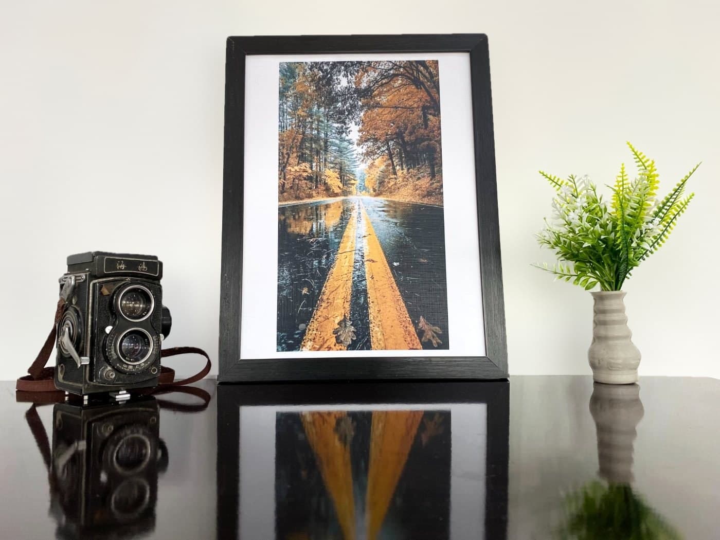 Autumn road print in a 12×16 black frame on a table against a plain wall